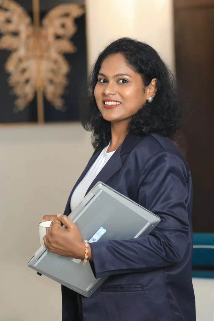 A smiling professional female website designer in Bhopal holding a laptop and coffee cup, wearing a dark blue blazer.