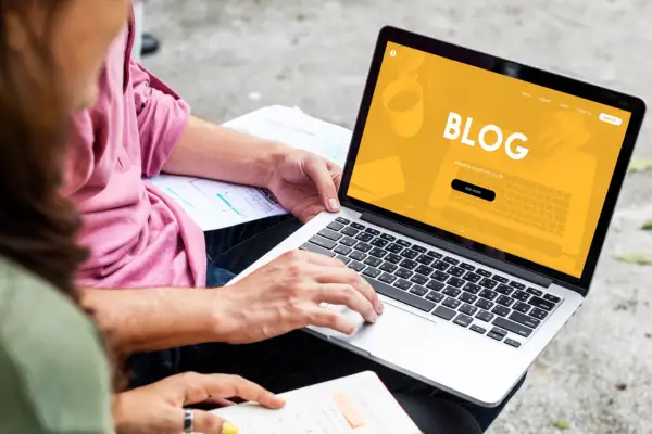 Person typing on a laptop reviewing old website content with a yellow blog screen displayed clearly outdoors.